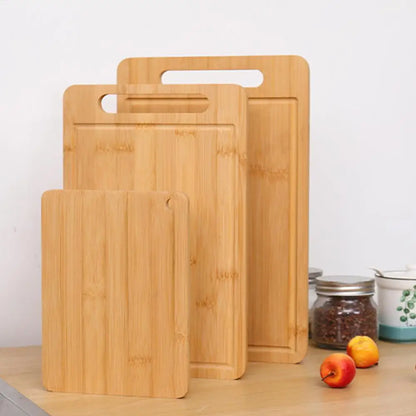 Set of three bamboo cutting boards on a wooden surface with fruits and jars in the background.